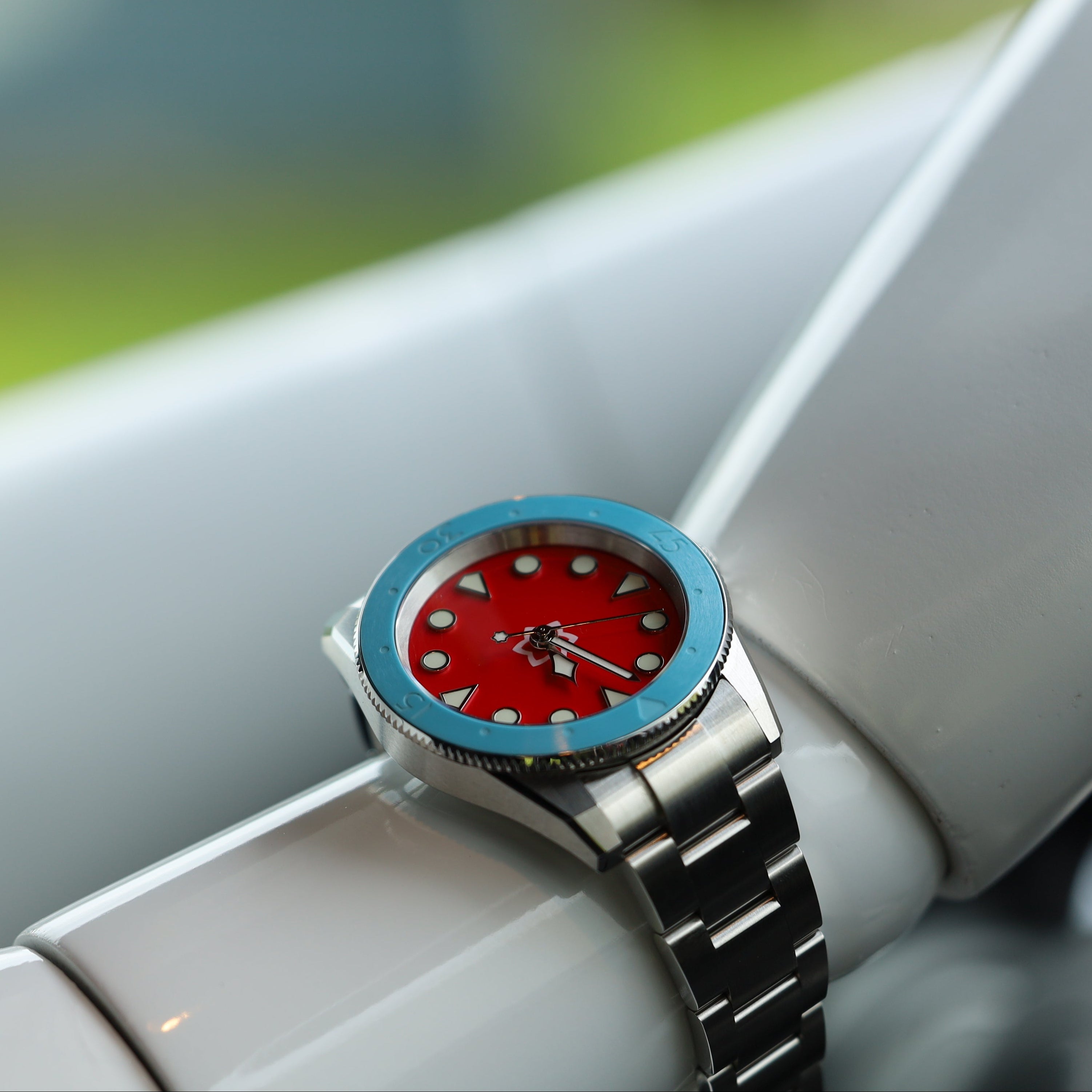 Wristwatch with a red face and silver strap on a car dashboard